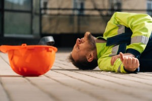 construction worker on ground holding arm and grimacing in pain